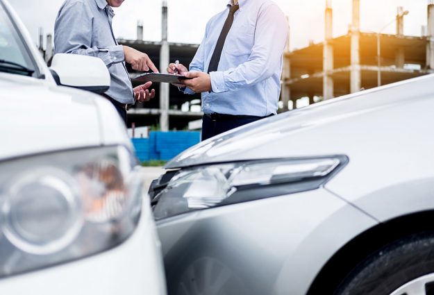 Insurance agent writing on clipboard while examining car after a Insurance agent writing on clipboard while examining car after accident claim being assessed and processed